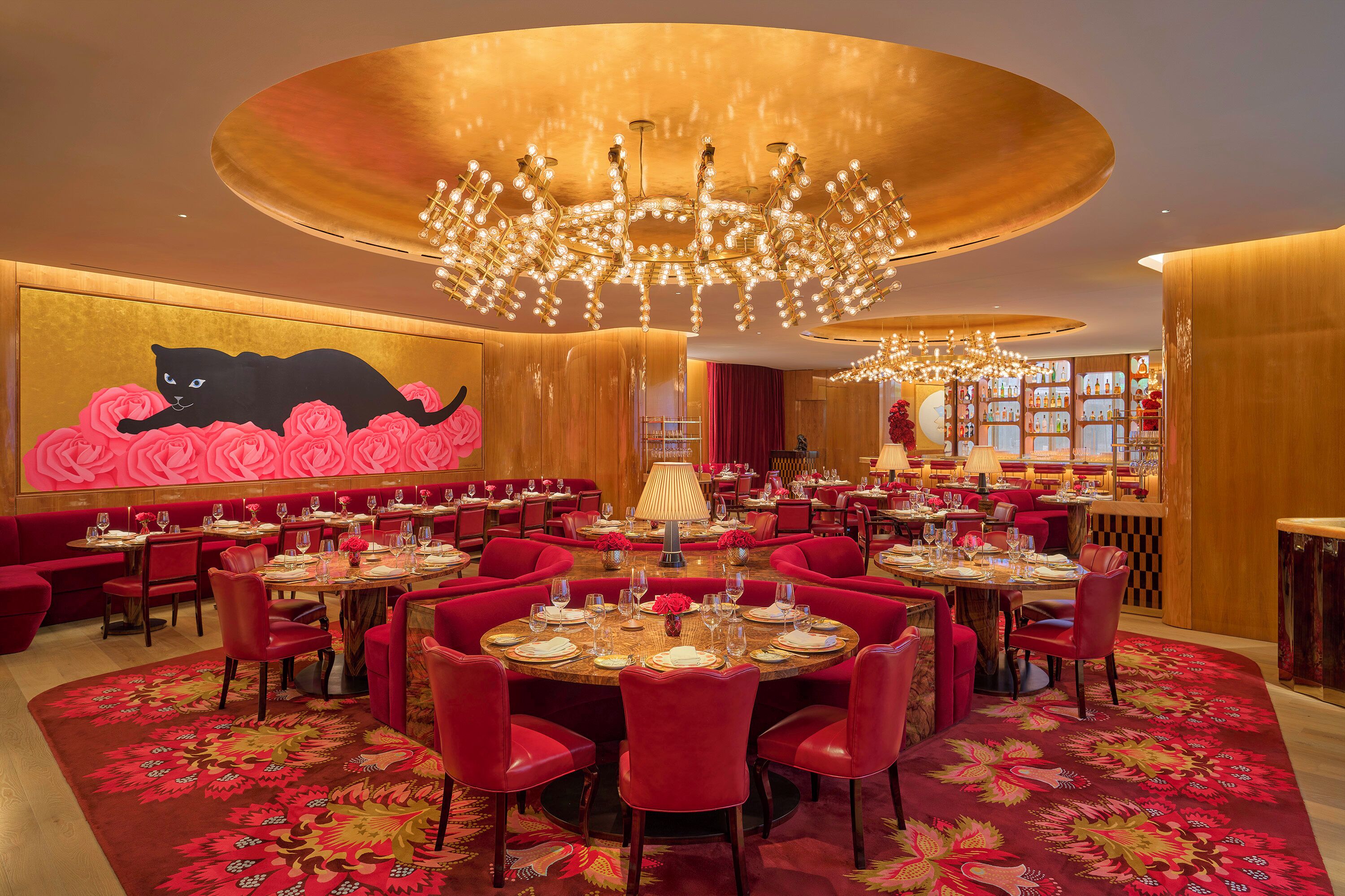 Uma sala de jantar luxuosa com mesas redondas, cadeiras vermelhas e um grande candelabro.