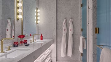A modern bathroom with a large mirror, vanity with gold fixtures, a shower area, and towels with initials.
