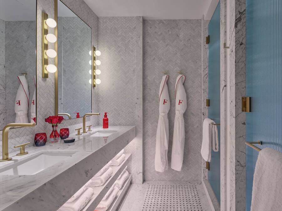 A modern bathroom with a large mirror, vanity with gold fixtures, a shower area, and towels with initials.