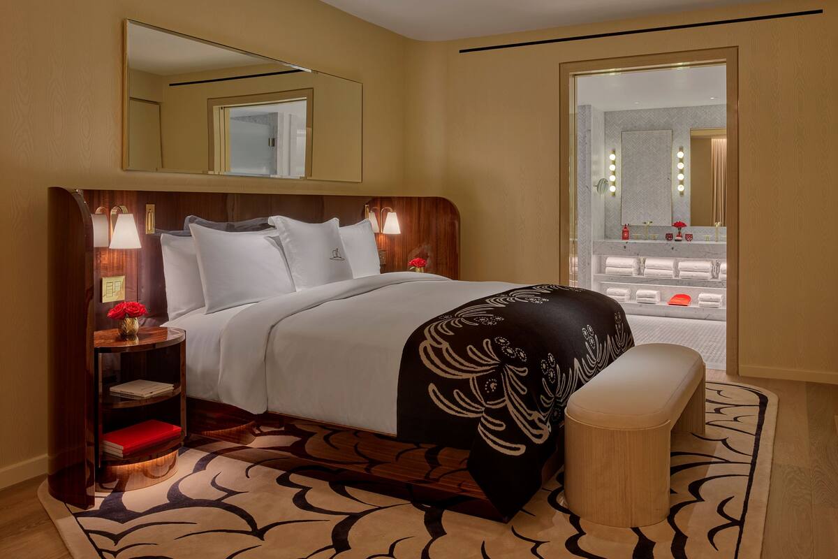 Habitación de hotel con una cama grande, mesitas de noche con lámparas, un espejo y vista al baño.