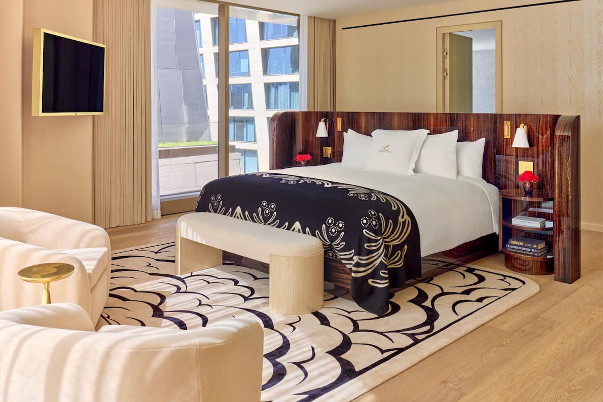 Una habitación de hotel moderna con una cama grande, un banco, un televisor y vistas de la ciudad a través de la ventana.