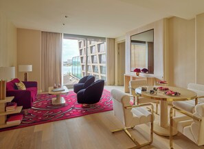 Une chambre d’hôtel moderne avec une grande fenêtre, un tapis rouge à motifs, une table à manger agrémentée d’un vase de fleurs et un canapé.