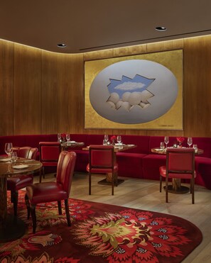 Un restaurant avec des banquettes rouges, des murs lambrissés et un grand tableau abstrait accroché au mur.