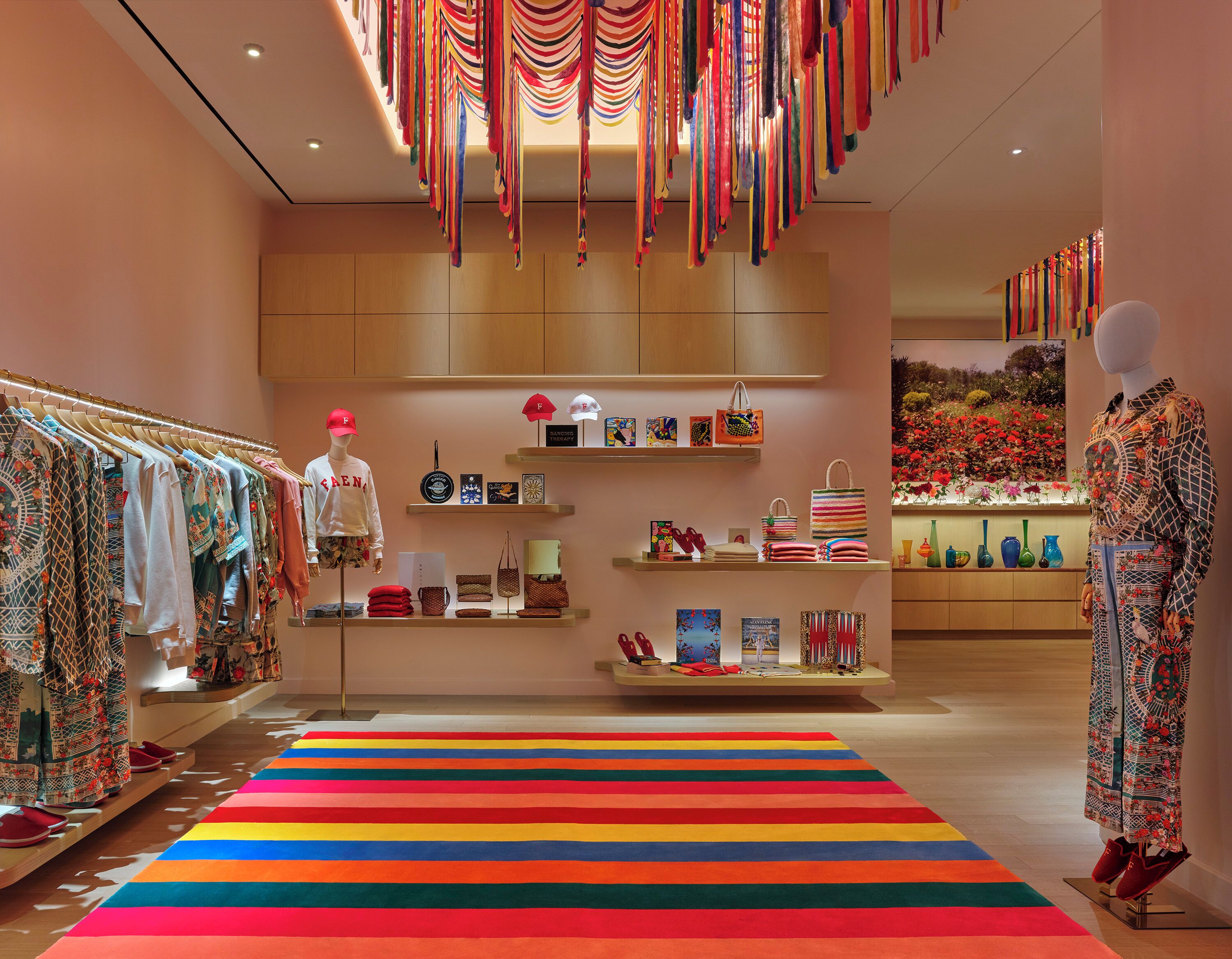 Uma loja boutique com um manequim, araras de roupa, prateleiras com bolsas e um tapete listrado e colorido.