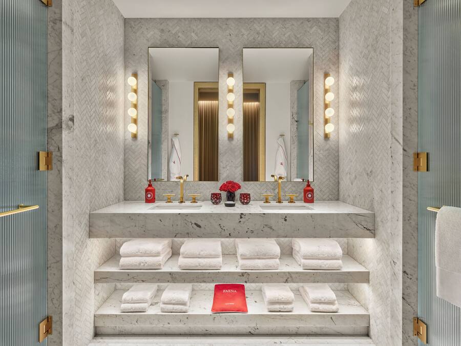 Une salle de bain moderne avec un lavabo en marbre, deux miroirs et un porte-serviettes où sont soigneusement pliées les serviettes.