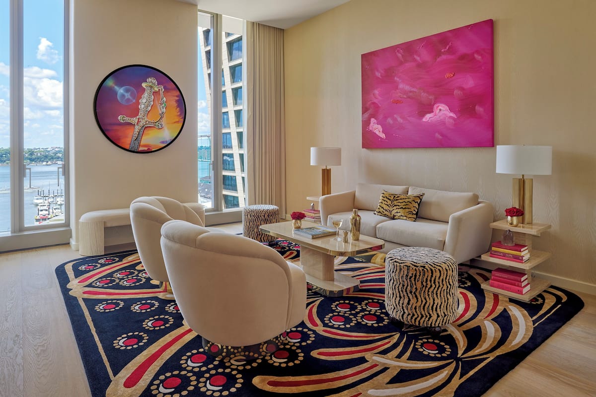Una sala de estar moderna con un ventanal grande, un sofá blanco, dos sillones, una mesita de centro y una alfombra colorida.
