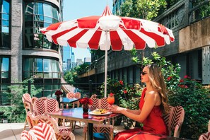 An outdoor seating area with a table, chairs, and a red and white striped umbrella. - Faena New York (New York)