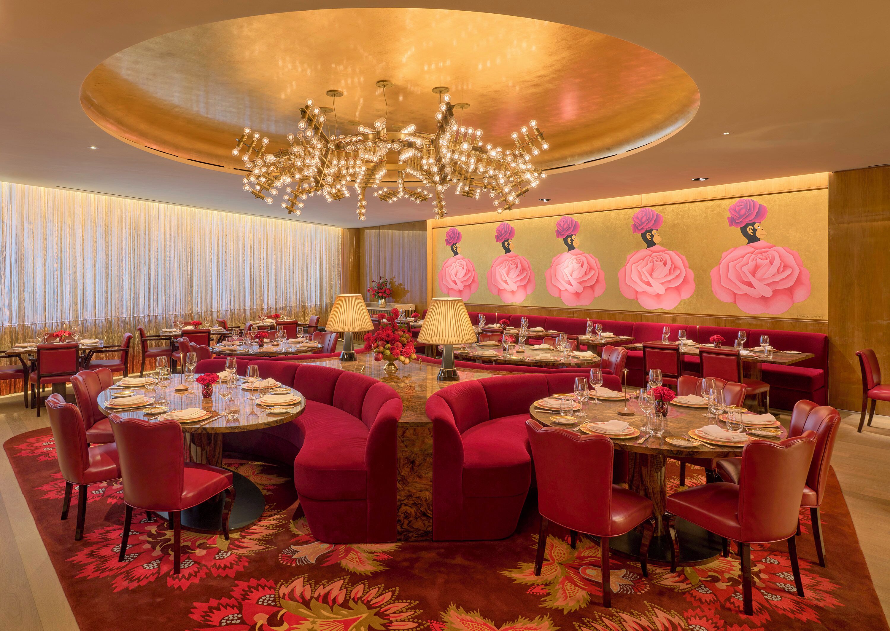 A luxurious dining area with round tables, red upholstered chairs, and a large chandelier.