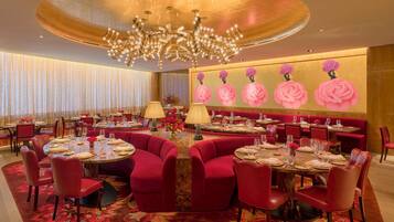 A luxurious dining area with round tables, red upholstered chairs, and a large chandelier.
