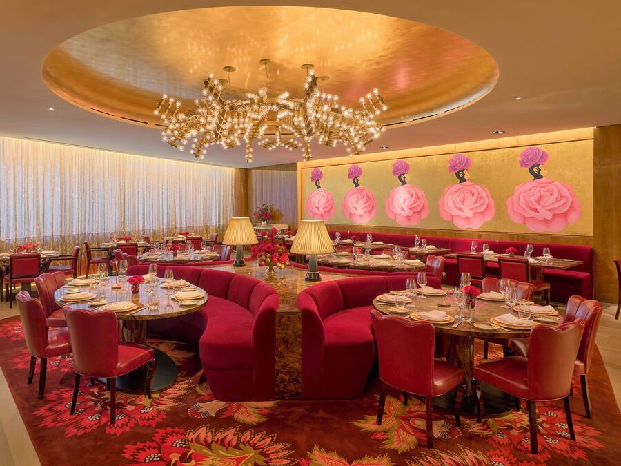 A luxurious dining area with round tables, red upholstered chairs, and a large chandelier.