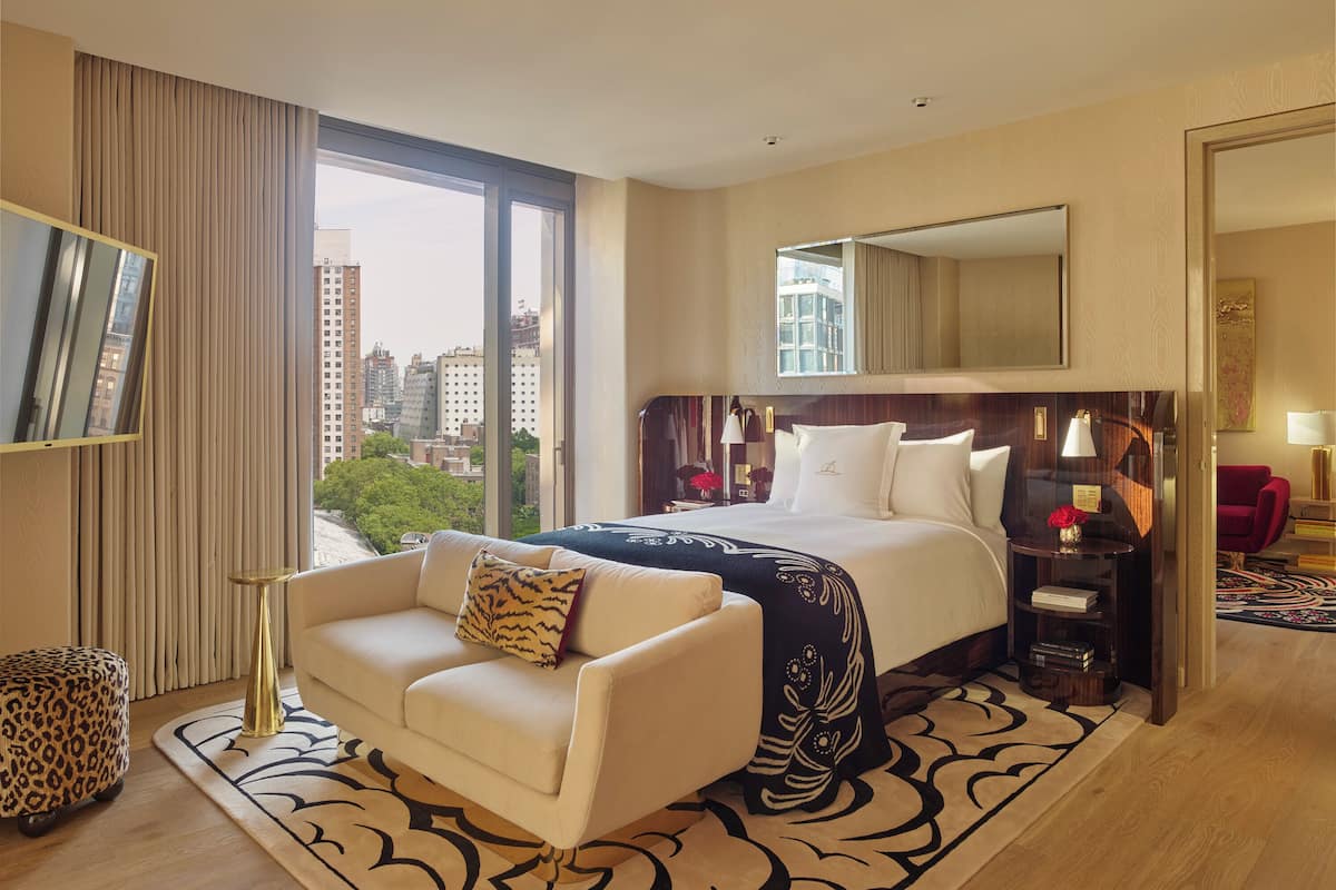 Habitación de hotel con una cama grande, un sofá, un televisor, un escritorio y vistas a la ciudad.