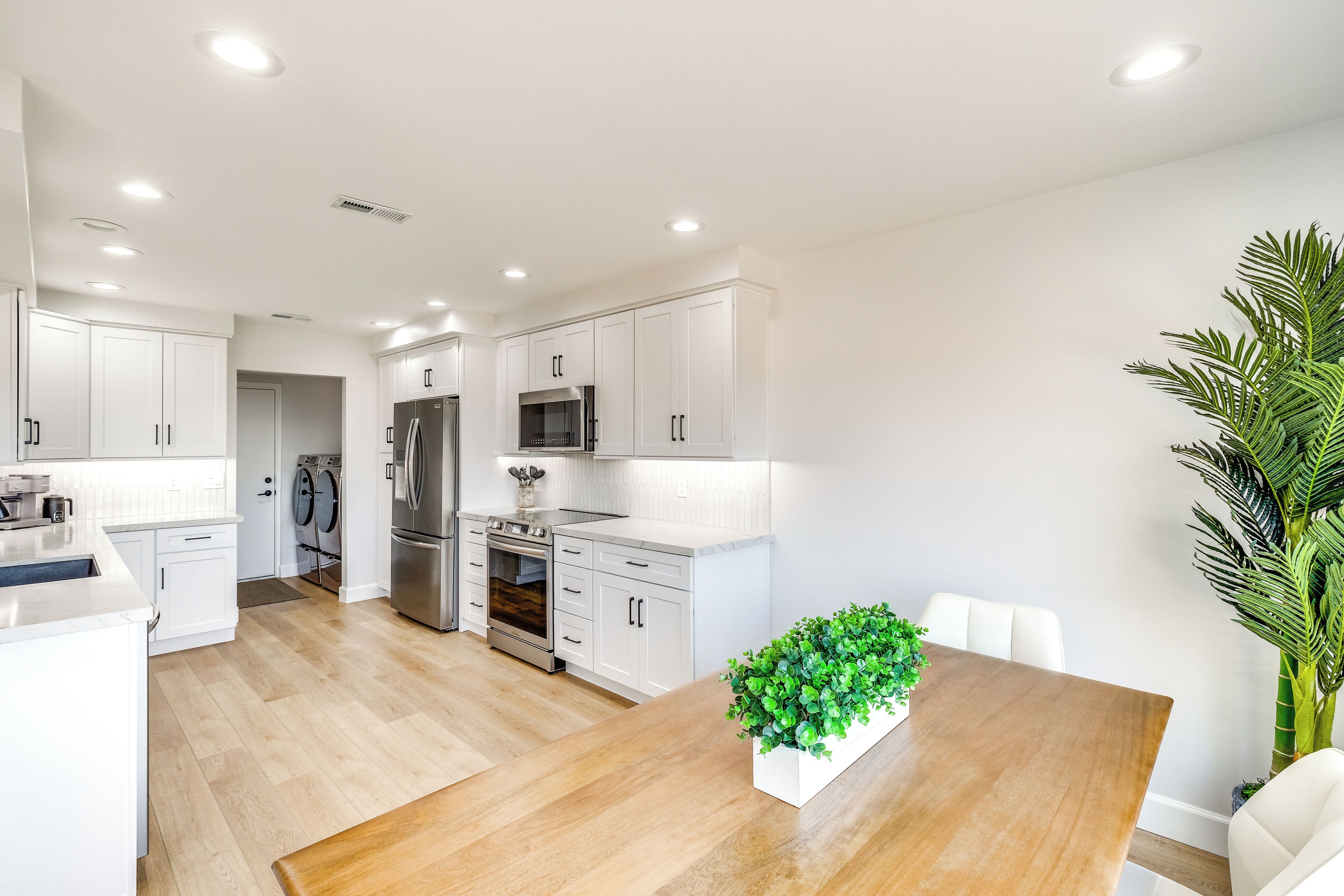 A modern kitchen with white cabinetry, stainless steel appliances, and a wooden dining table with a green centerpiece.