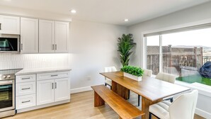 Een moderne keuken met witte kastjes, een inbouwmagnetron en een houten eettafel met stoelen.