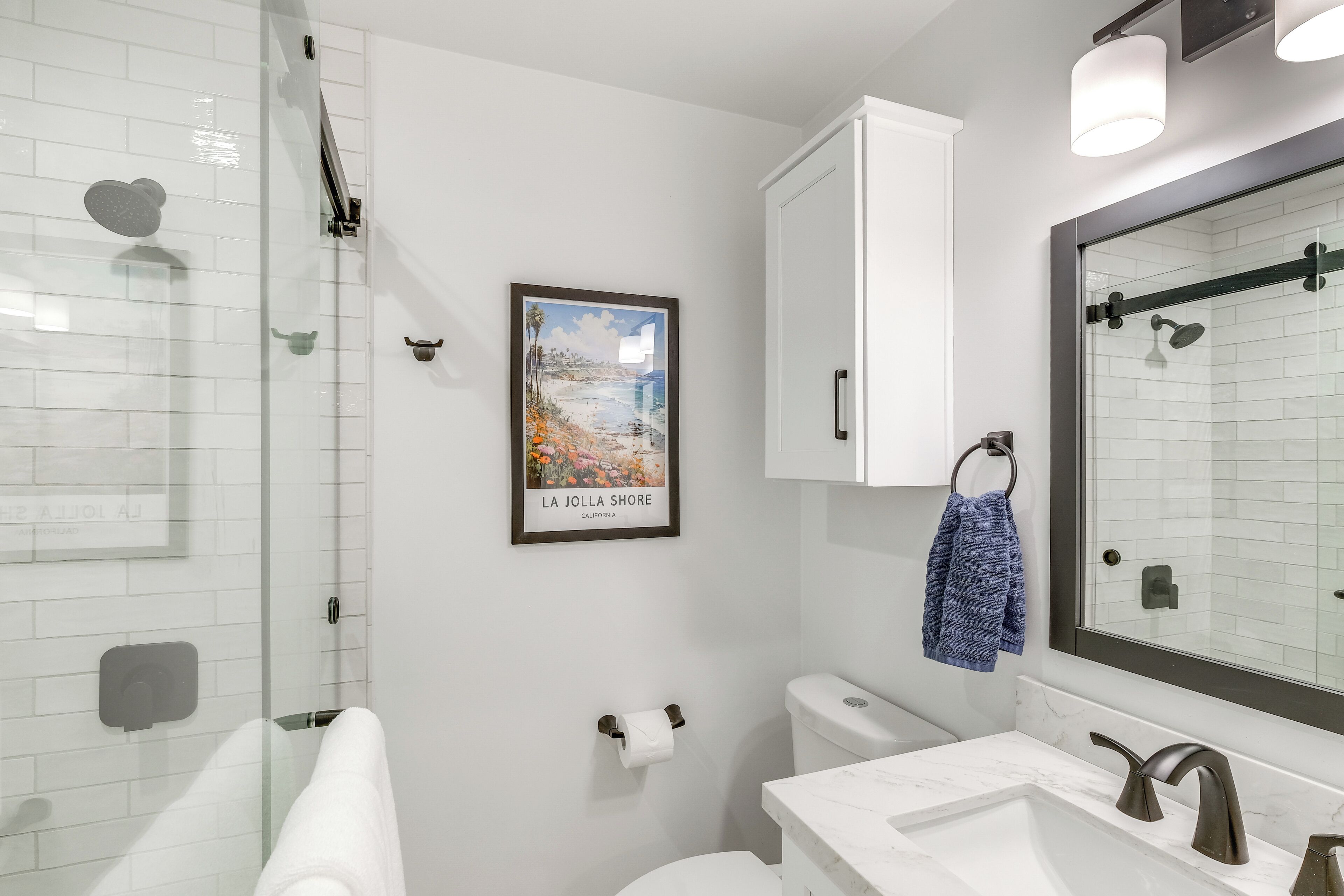 A modern bathroom with a glass shower enclosure, a white toilet, a sink with a marble countertop, and a large mirror.