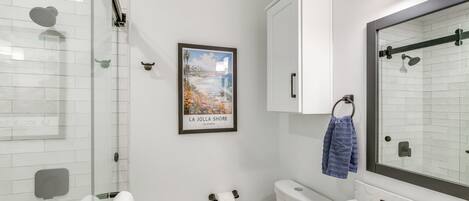 A modern bathroom with a glass shower enclosure, a white toilet, a sink with a marble countertop, and a large mirror.