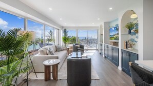 Un vaste espace de vie doté d’une grande fenêtre offrant une vue sur un port de plaisance, d’un canapé, d’une table basse et d’un coin repas avec vue.