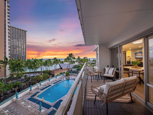 A rooftop pool with lounge chairs and a dining area overlooking a sunset.