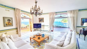 A living room with a sofa, a television, a chandelier, and a view of the sea. - Villa Furore... a breathtaking view! (Campania)