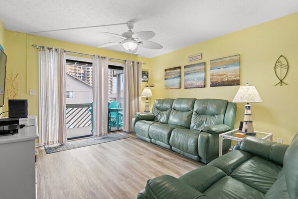 Relax in this stylish living room with a sofa, armchair, and ceiling fan, offering a view of the surrounding area through the sliding glass door.