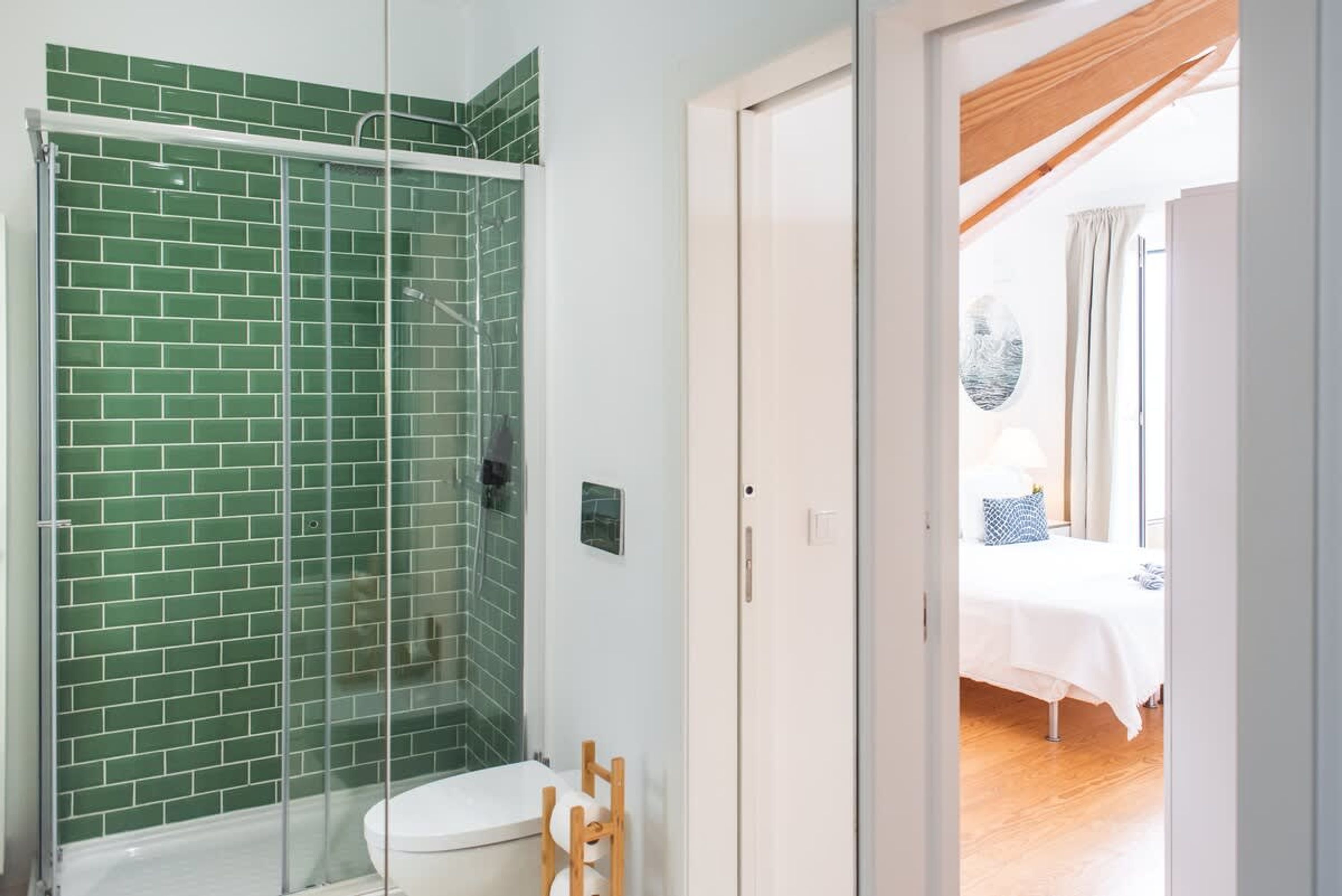 A bathroom with a green-tiled shower enclosure and a white toilet.