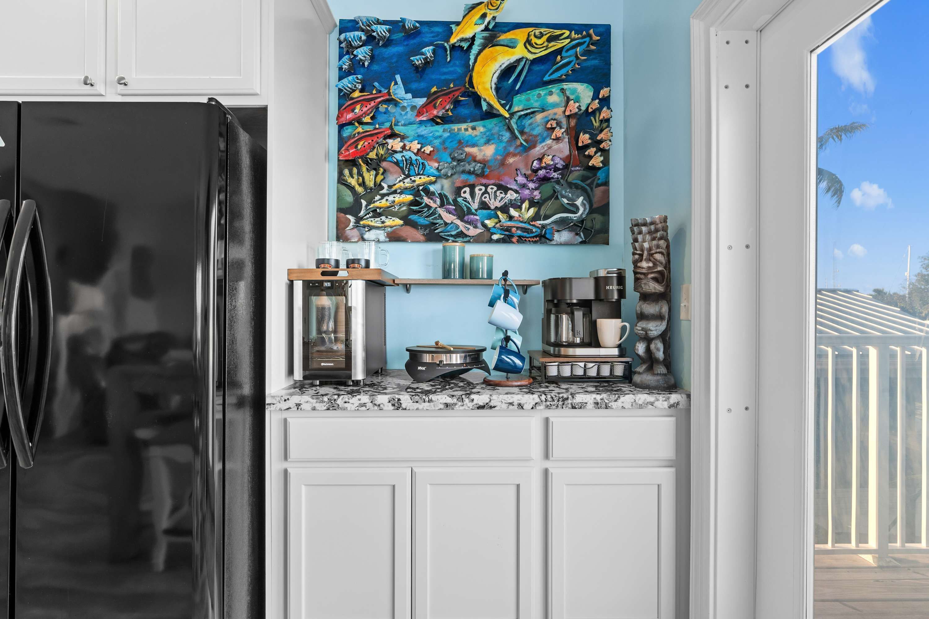 Eine Küche mit einem schwarzen Kühlschrank, einer Kaffeemaschine und einem farbenfrohen Wandbild.
