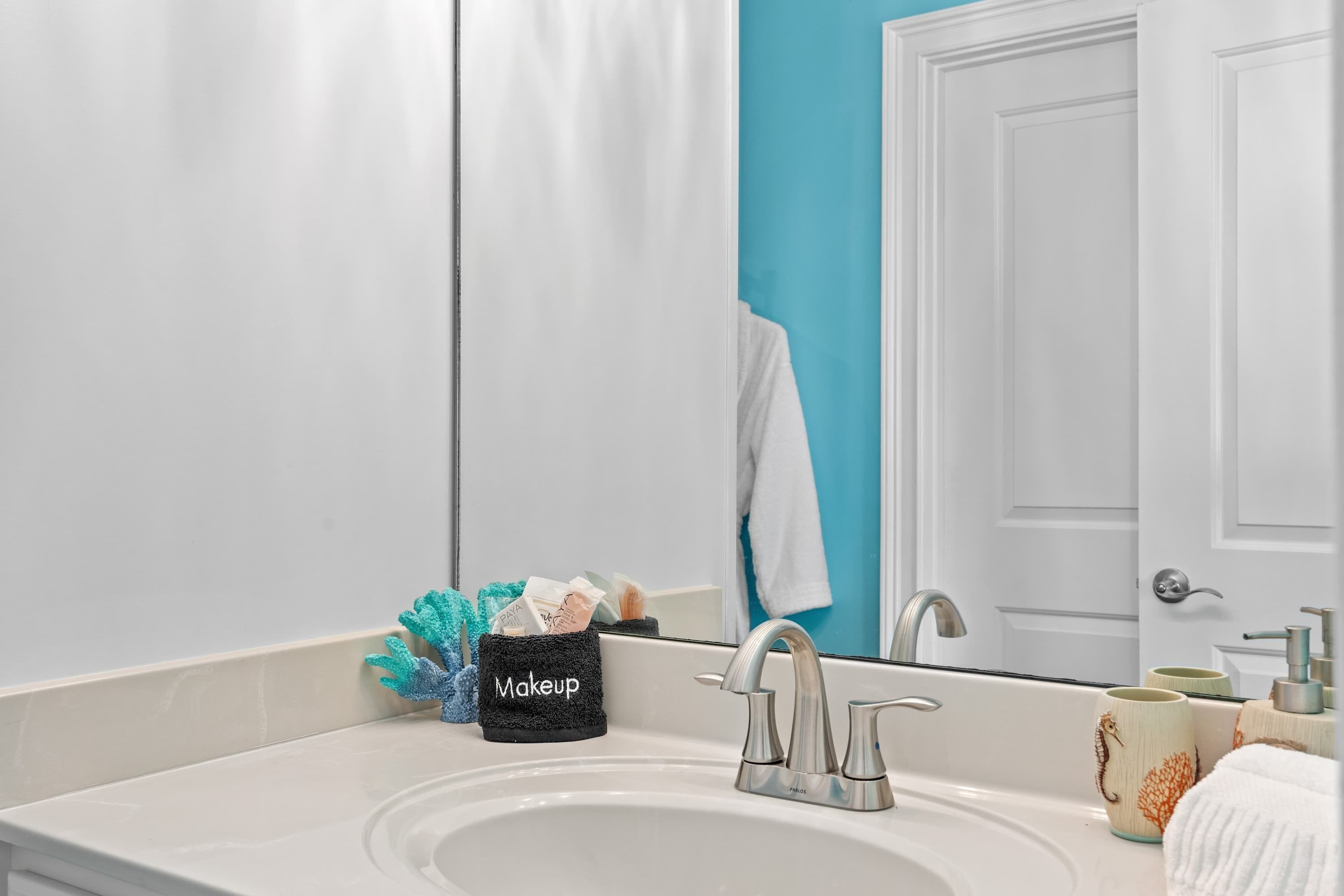 A bathroom with a white sink, a mirror, a makeup organizer, and a towel rack.