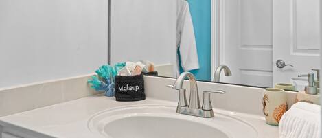 A bathroom with a white sink, a mirror, a makeup organizer, and a towel rack.