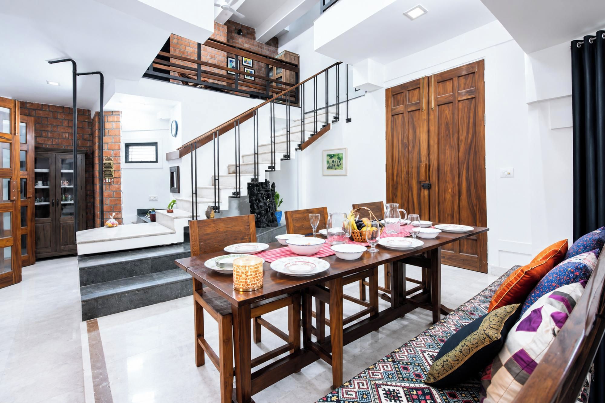 A spacious dining area with a high ceiling, a staircase, and a wooden dining table set for a meal.