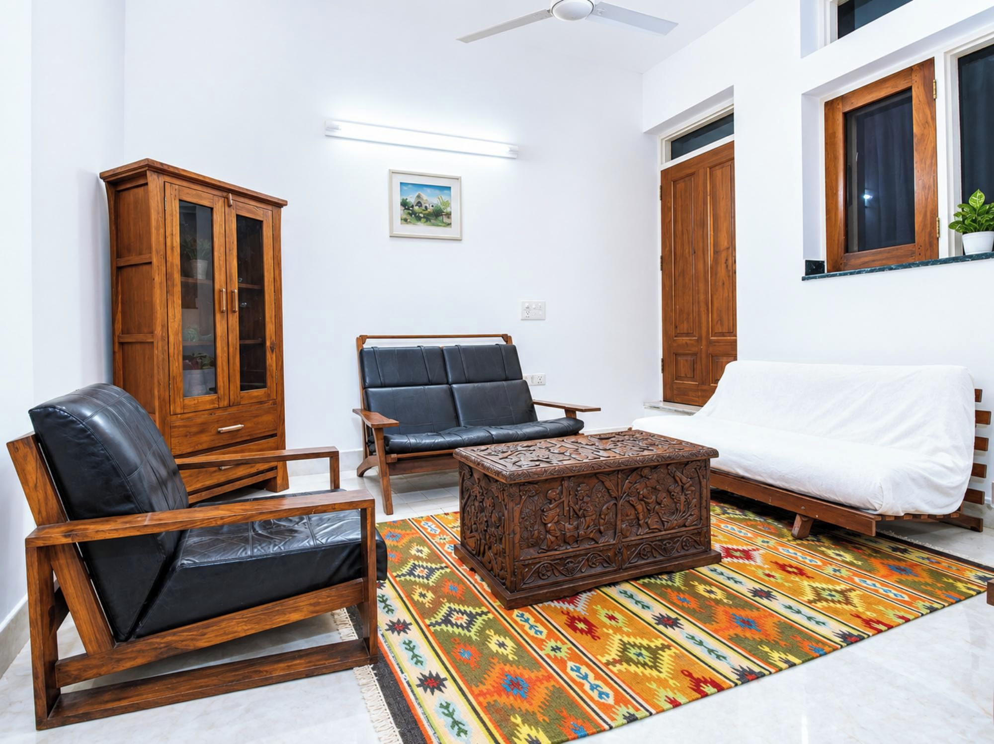 A living room with a sofa, armchair, wooden cabinet, and a patterned rug.