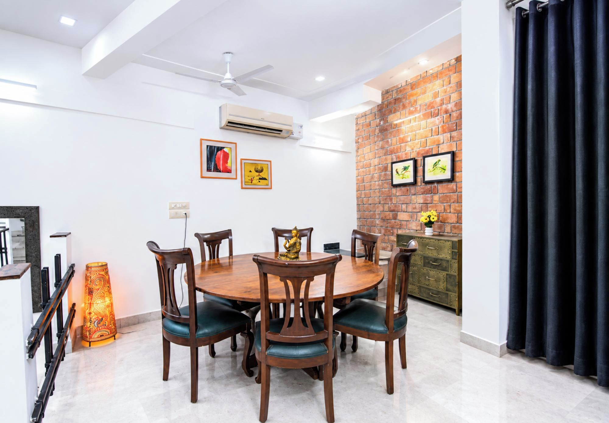 A dining area with a round table, six chairs, and a decorative Buddha statue.