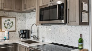 Una cucina con elettrodomestici in acciaio inossidabile, mobili in legno, uno schienale in marmo e una bottiglia di vino sul bancone.