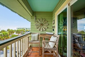 Ein Balkon mit zwei HolzstĂŒhlen, einer Wanddekoration und Blick auf die StraĂe sowie auf Palmen.