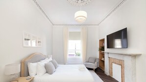 Une chambre à coucher comprenant un lit, une table de chevet, une lampe, une télévision, une cheminée et une vue sur l’extérieur.