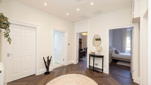 Un couloir avec un tapis rond de couleur beige, des portes blanches, une console noire avec un miroir et, au fond, un lit.
