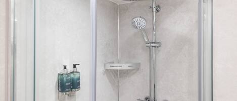 A modern shower with a handheld showerhead and a wall-mounted faucet, glass shower enclosure, and two bottles of shampoo on a wall-mounted soap dispenser.