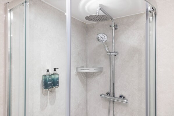 Ducha moderna con cabezal de ducha de mano y grifo empotrado, cerramiento de ducha de vidrio y dos botellas de champú en un dispensador de jabón de pared.
