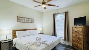 A hotel room with a bed, a ceiling fan, a TV, a dresser, and a window with curtains.