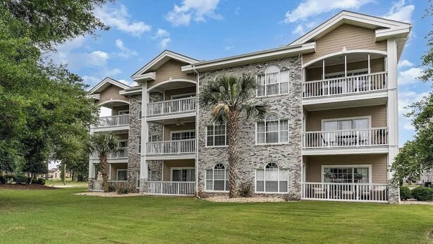 A multi-story hotel with balconies, stone facade, and a well-maintained lawn.