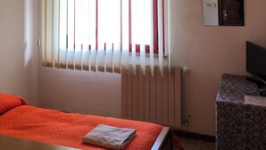 Una stanza con un letto, un tavolo, una televisione e una finestra con persiane verticali.