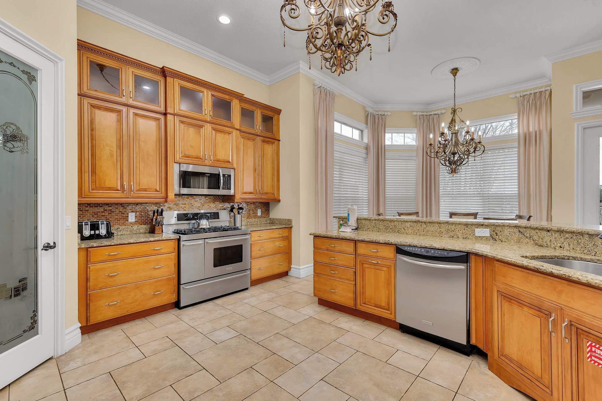 A kitchen with wooden cabinets, granite countertops, stainless steel appliances, and a chandelier.