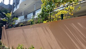 Un edificio con parete esterna color crema, un balcone con piante in vaso e vista su un edificio adiacente.