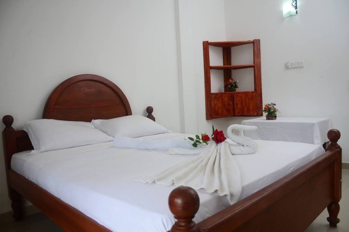 A neatly made bed with white linens, a wooden headboard, and a decorative towel with a rose.