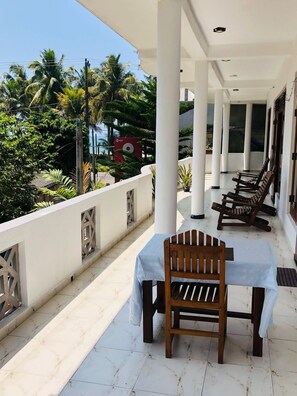 A covered outdoor seating area with a table and chairs, surrounded by white pillars and a view of palm trees. - Viva la vida (Hikkaduwa)