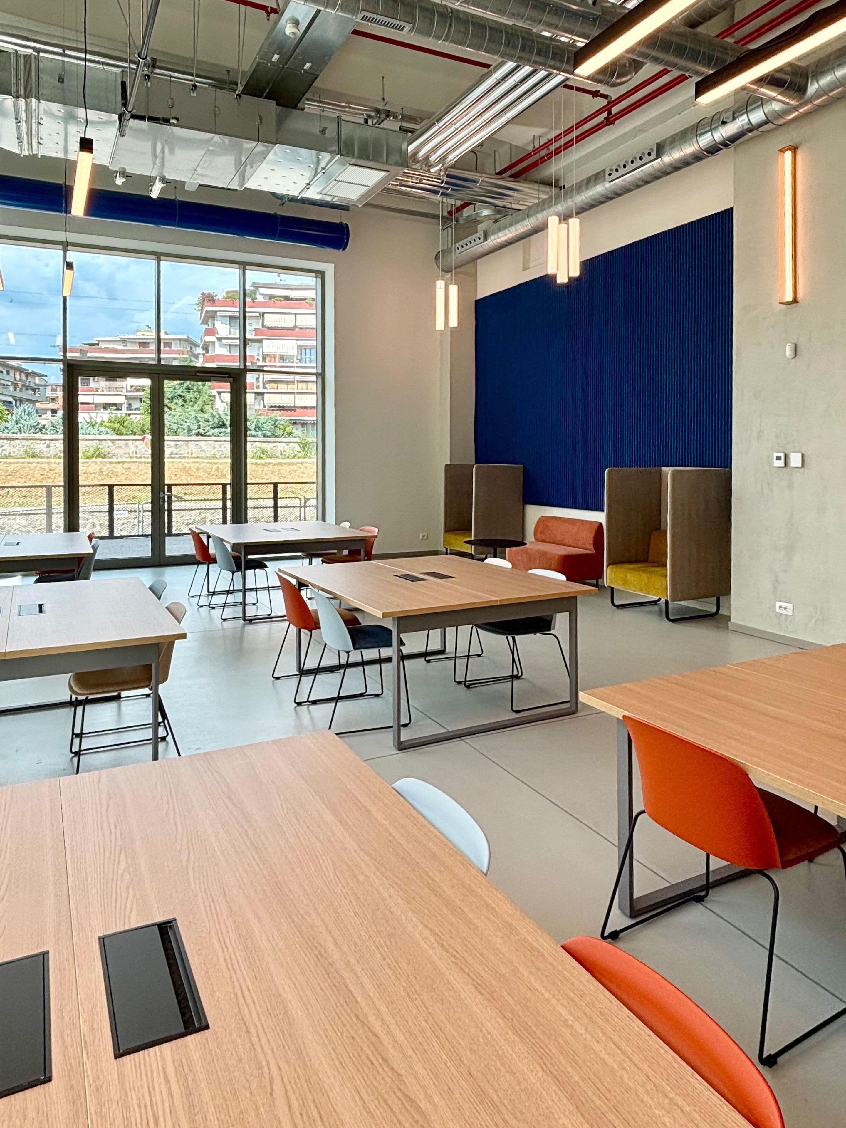 A modern conference room with large tables, chairs, and a view through the glass doors.