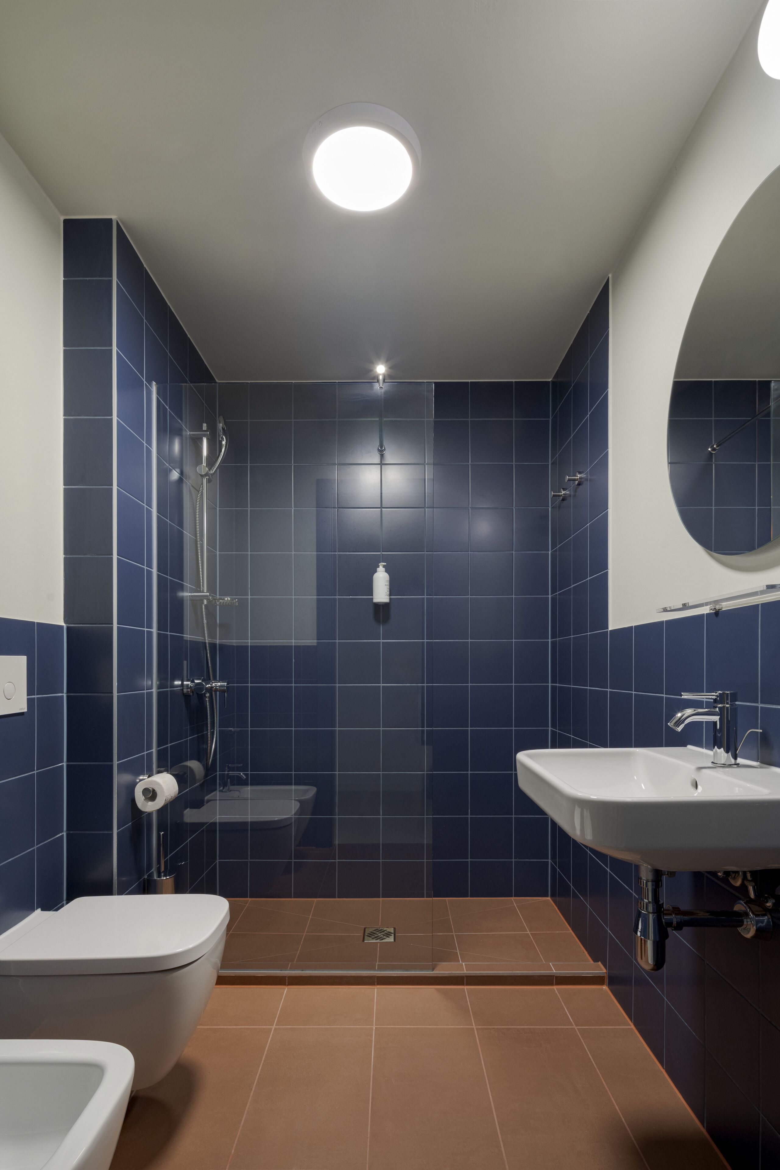 Une salle de bain moderne avec des carreaux bleus, un lavabo blanc, des toilettes et un espace douche.