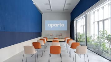 A conference room with rows of chairs facing a projection screen displaying "aparto".