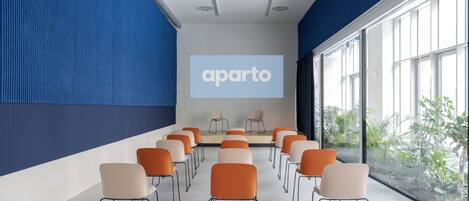 Un salón de conferencias con filas de sillas mirando hacia una pantalla de proyección que muestra “aparto”.