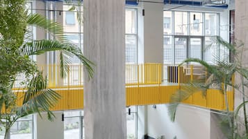 Un interior moderno con un pilar central de hormigón, barandillas amarillas y una zona de estar con sofá amarillo.