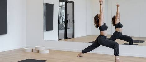 Un estudio de yoga con un espejo grande, tapetes de yoga negros y suelo de madera.