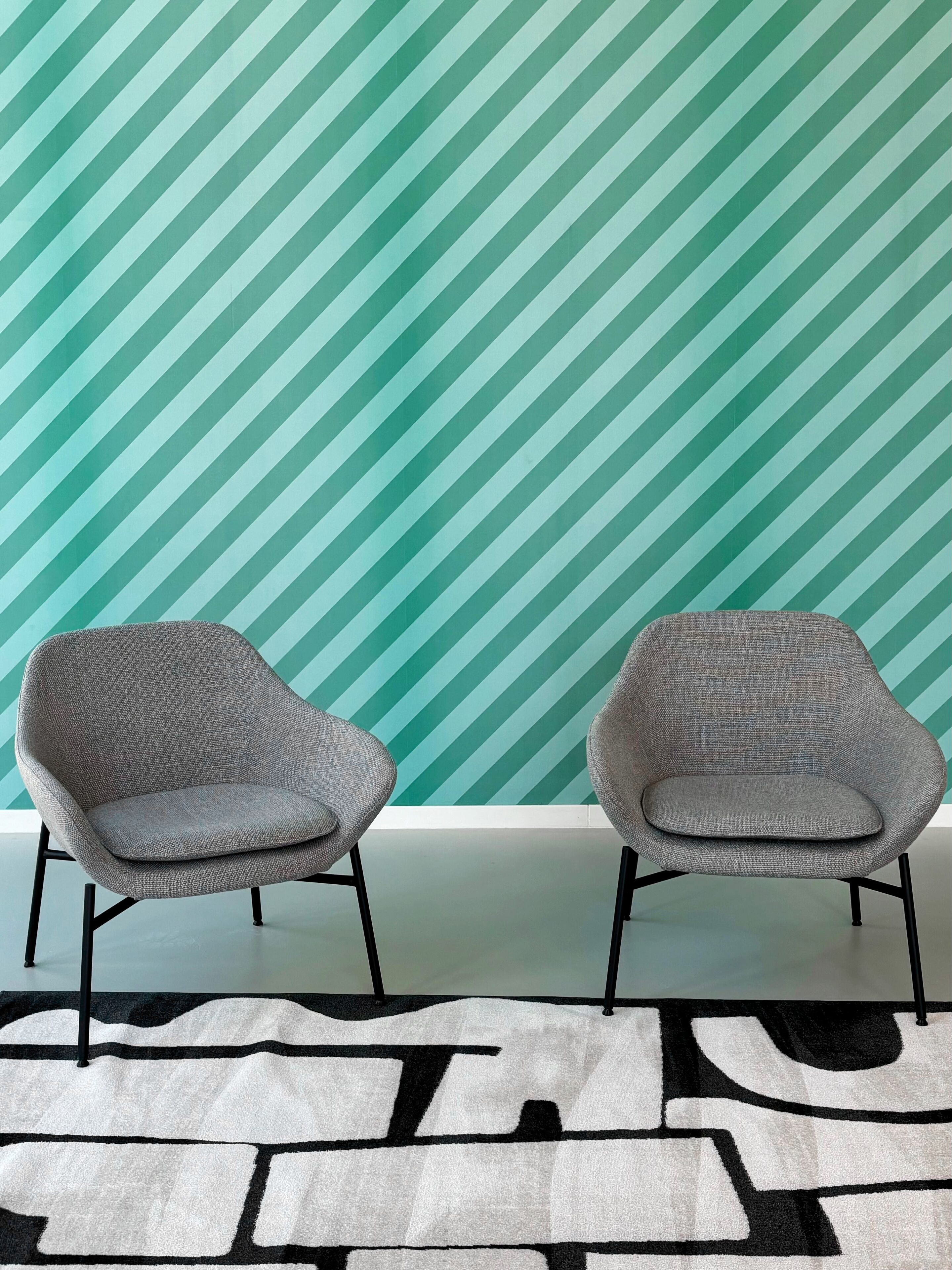 Two grey armchairs with black legs against a teal striped wall.